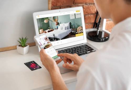 Επισκέπτης κάνει online κράτηση ξενοδοχείου μέσω laptop και smartphone